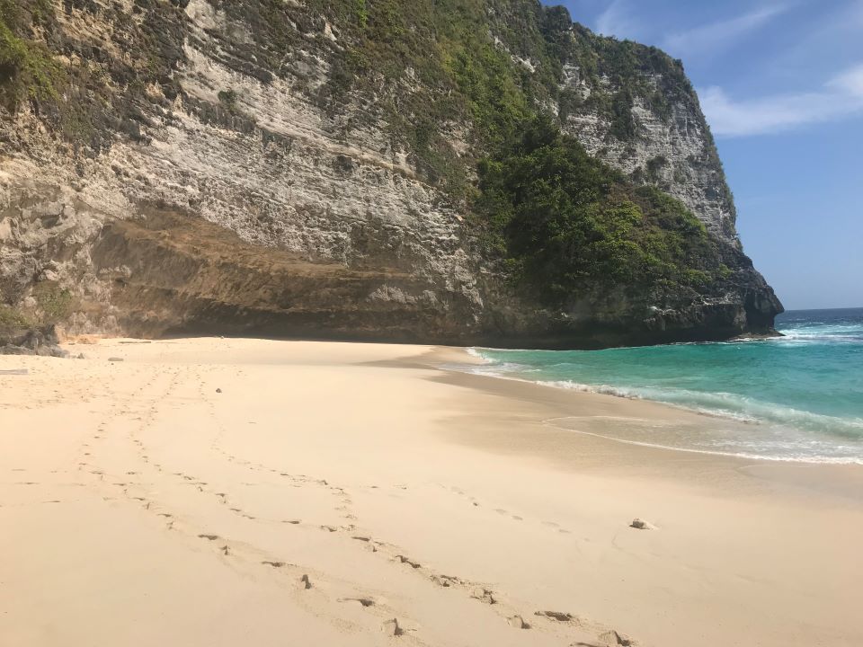 ruta por indonesia vistas de playa de arena blanca con agua de mar turquesa con una pared enorme enfrente